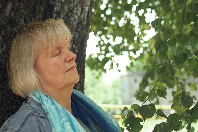 Märchenexpertin Elke Fischer-Wagemann lehnt mit geschlossenen Augen gegen einen Baumstamm.