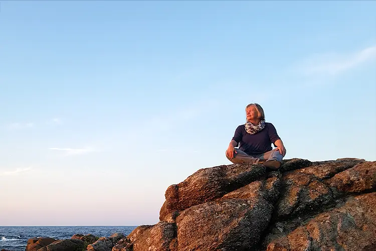 Die Märchenexpertin Elke Ficher-Wagemann sitzt auf einem Felsen in der Abendsonne und schau nach rechts in die Ferne.